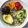 Quinoa salad with avocado and chia seeds in a bowl, garnished with fresh herbs.
