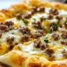 Sausage gravy crescent roll breakfast pizza topped with cheese and herbs.