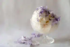 Scoop of lavender ice cream in a cone garnished with lavender sprigs
