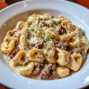 Plate of cheesesteak tortellini with creamy Parmesan sauce and garnished parsley.