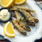 Platter of crispy Spanish-style fried sardines garnished with herbs.