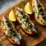 Lemon-garlic sardine toasts served on a wooden board.