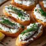 Sardine Goat Cheese Crostini topped with herbs on a wooden serving board.