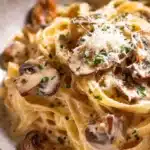 Bowl of creamy mushroom pasta topped with fresh herbs and grated cheese
