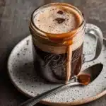 A cup of protein coffee with a scoop of protein powder beside it.