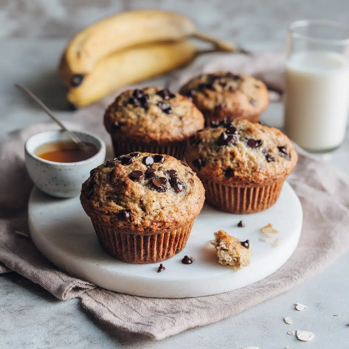 Vegan banana chocolate chip muffins served on a wooden board with coffee and fresh bananas